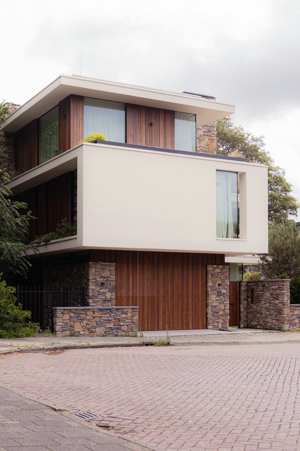 Modern house with wood, stone, and render under a cloudy sky.