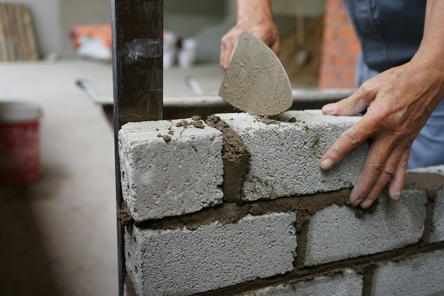 Construction worker's hands laying mortar and concrete blocks for a wall.
