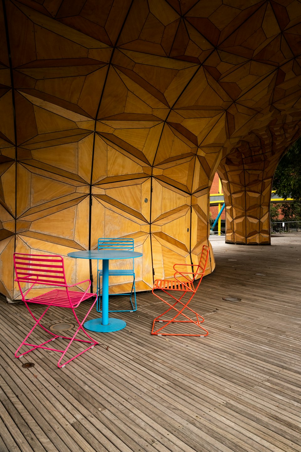 Colorful metal chairs sit on a deck near a wooden structure.