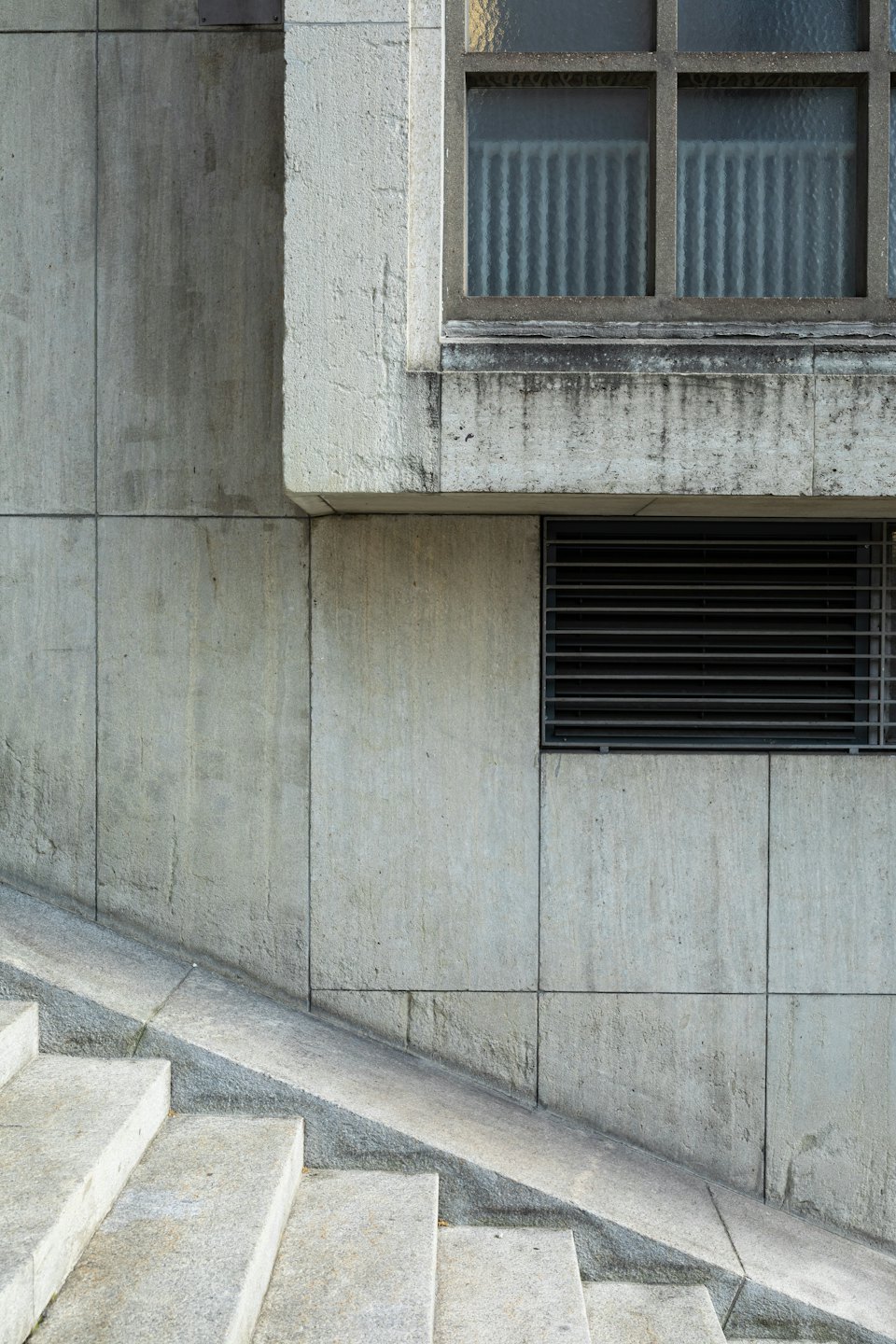 Textured concrete wall with a window and metal vent.